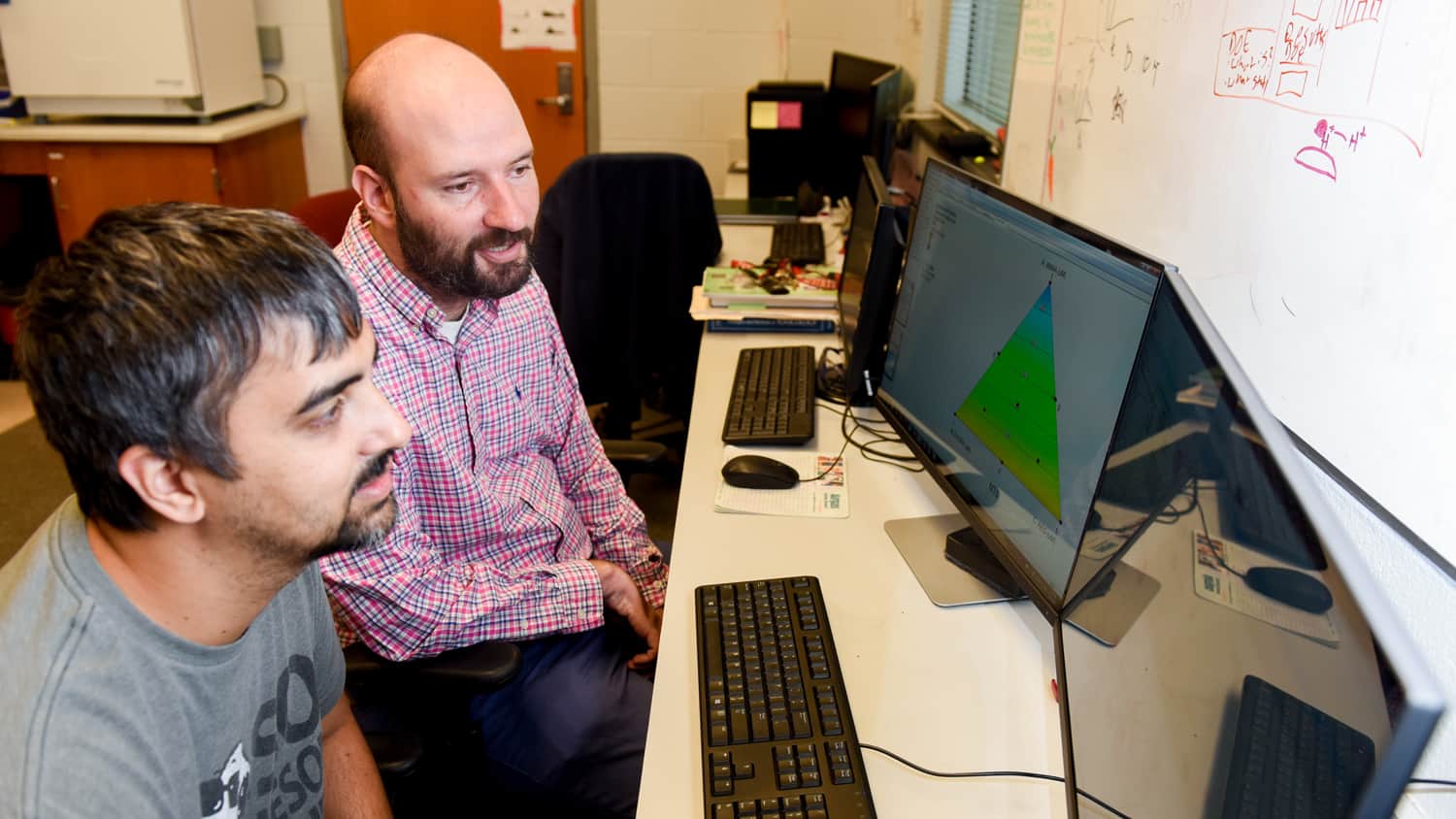 Michael Bereman (right) and graduate student Josh Beri look at a computer in his lab in 2017.
