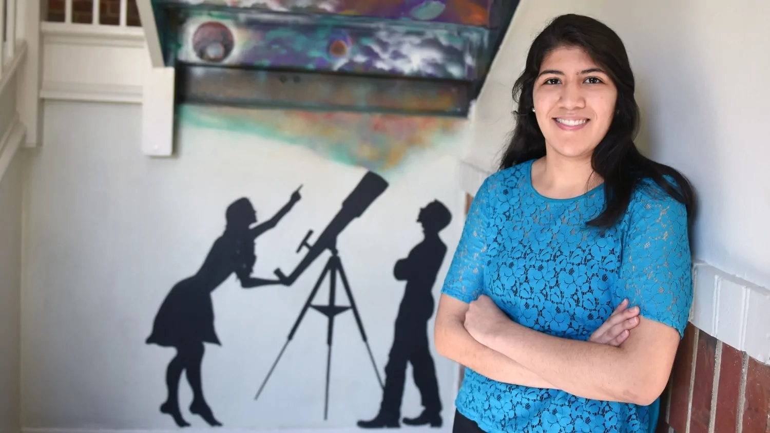 Paola Rivera in front of a painted silhouette of a man and woman at a telescope