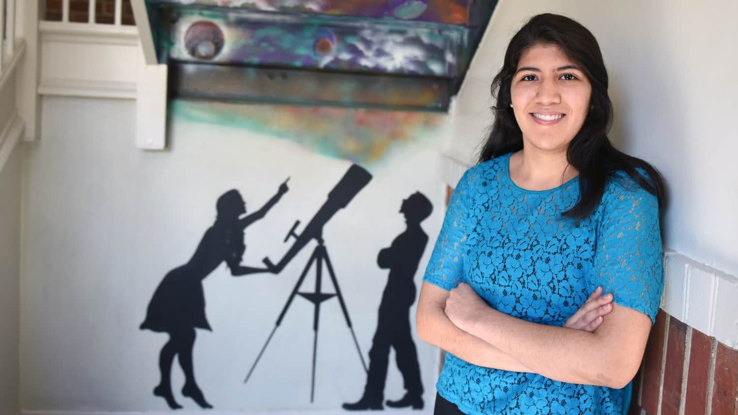 Paola Rivera in front of a painted silhouette of a man and woman at a telescope