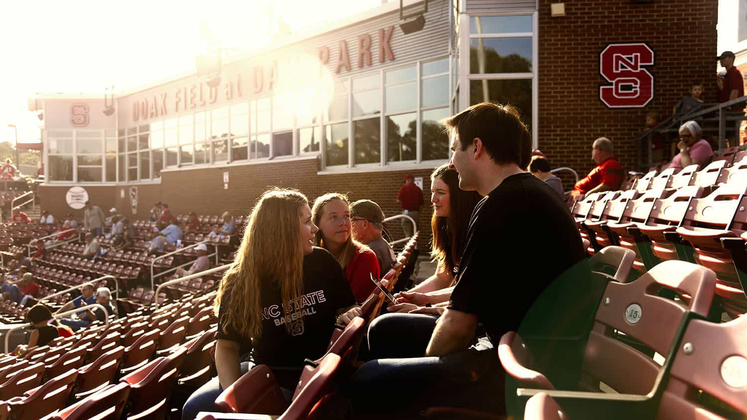 Students collaborating around laptop in baseball stadium stands
