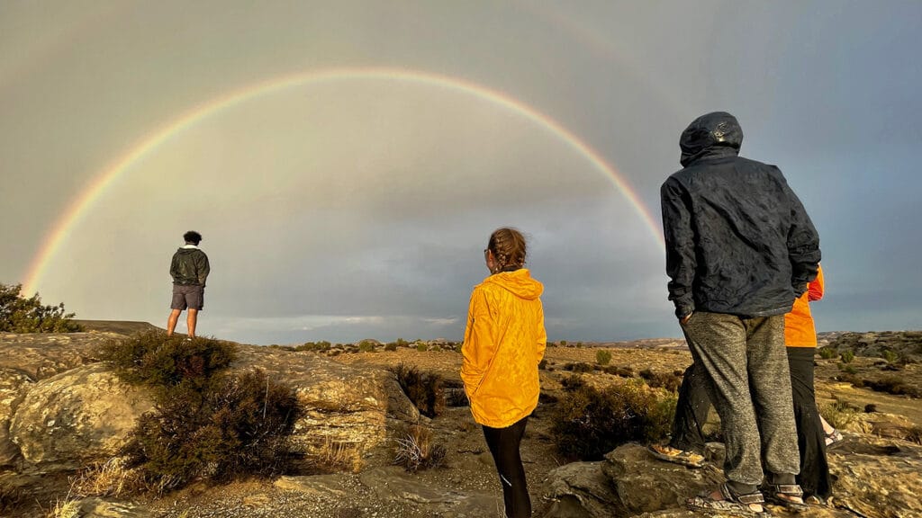 Several people look at a rainbow in the sky