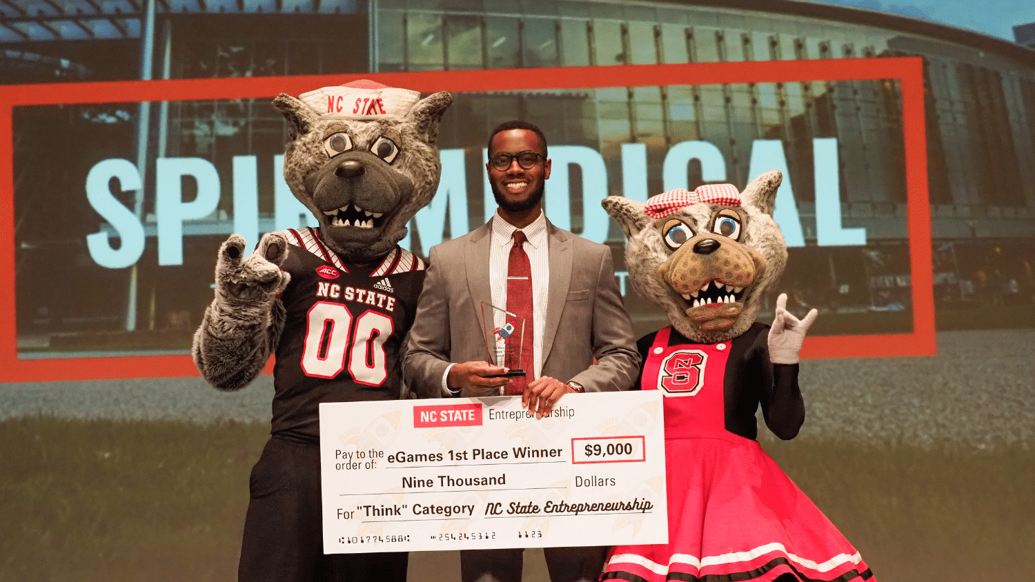 The 2022 eGames winner receives his cash prize with Mr. and Ms. Wuf on either side.