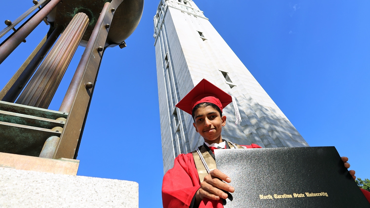 Madhusudan Madhavan holds his diploma at the base of the Belltower.
