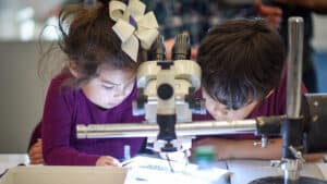 Two young children look at a sample under a microscope