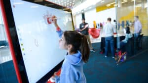 A young girl draws on a smartboard.