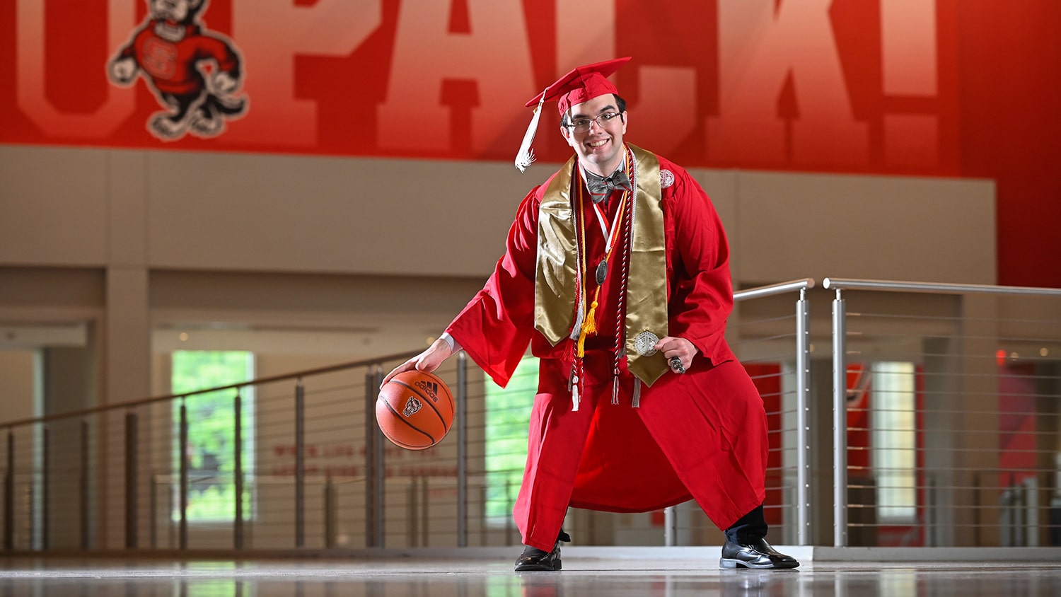 Billy Fryer dribbles a basketball inside Reynolds Coliseum while wearing his graduation cap and gown