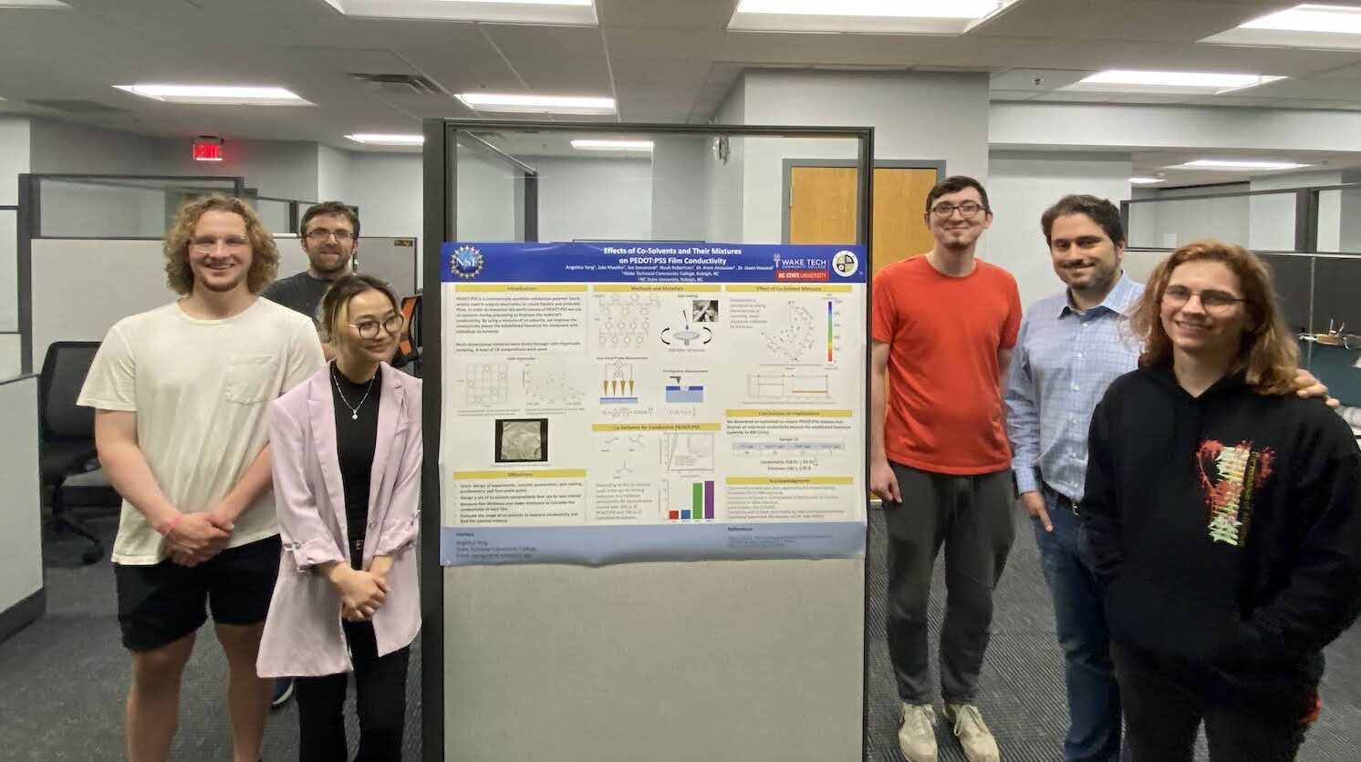 Students and faculty gather with a research poster