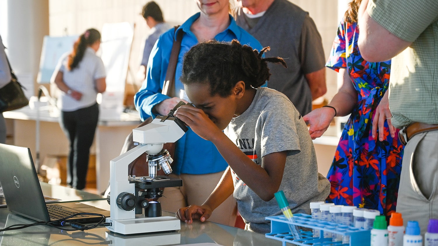 A young girl looks through a microscope at the 2023 State of the Sciences event