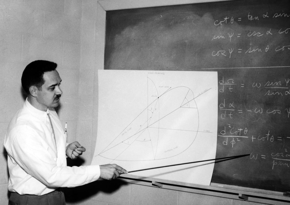 A black and white photo of Raimond Struble pointing at an equation on a blackboard