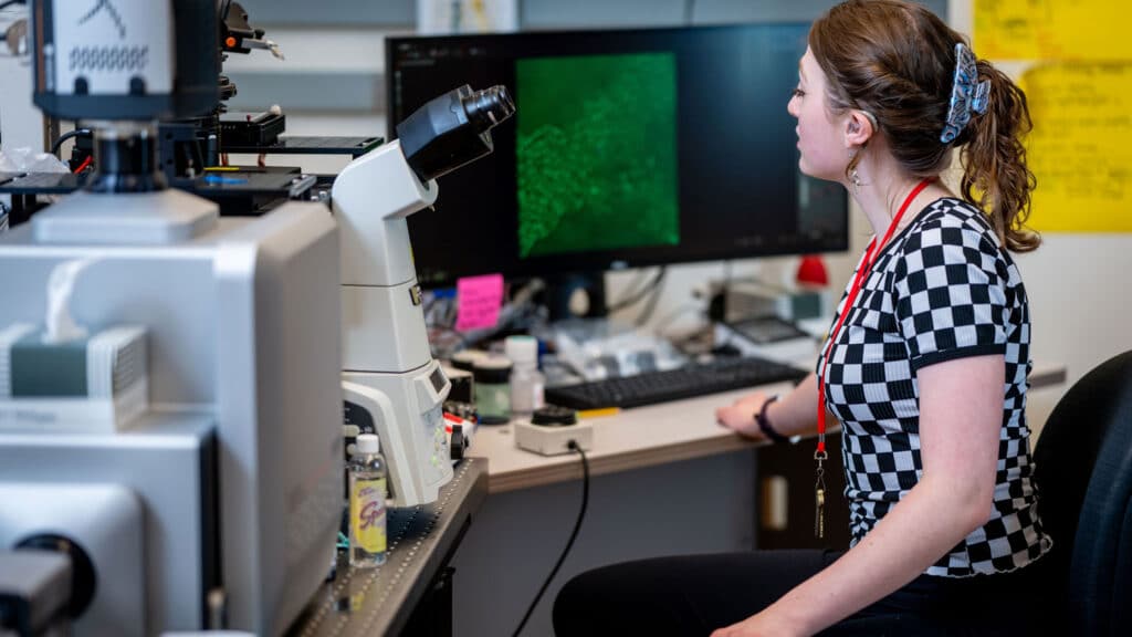 Kaelyn Coate sits at a desk with a microscope and computer screen