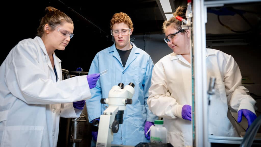 Mary Wang, Adam Nahor and Sierra Hunter stand around a microscope