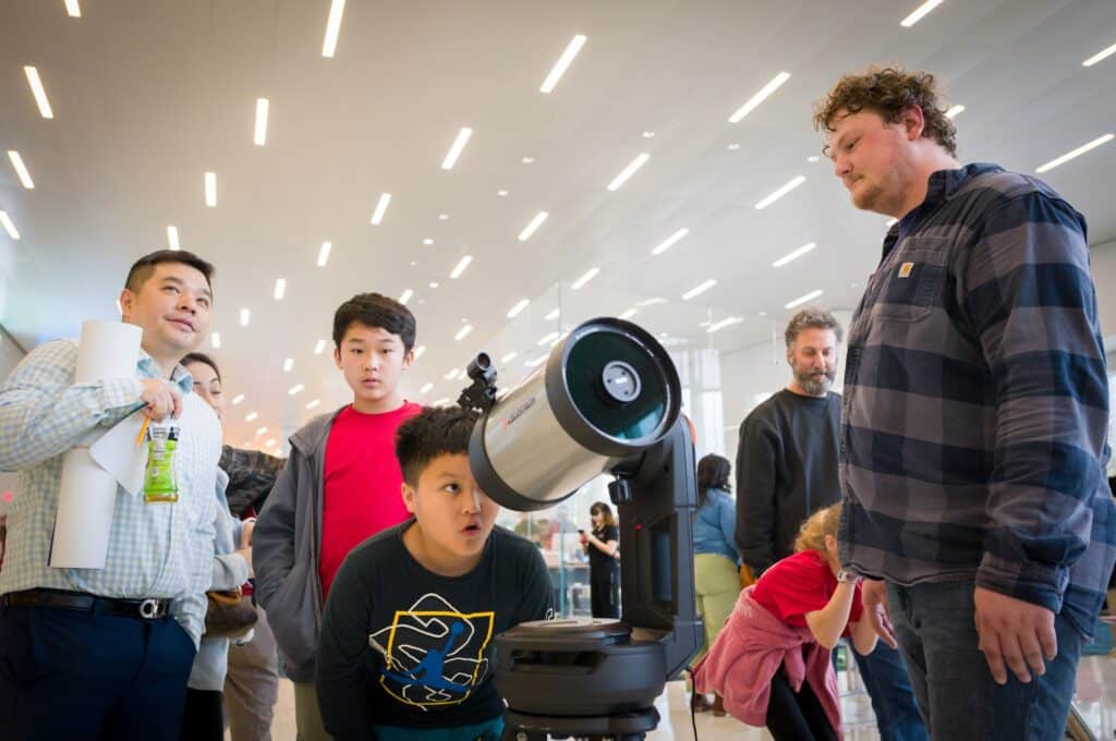 A child looks through a telescope as adults look on