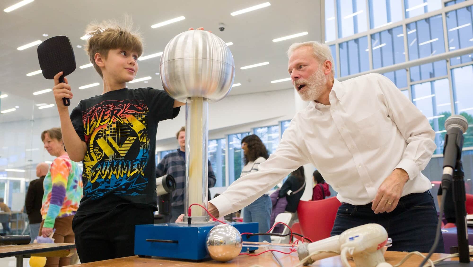 A child places his hand on a Van de Graaff generator while an adult looks on
