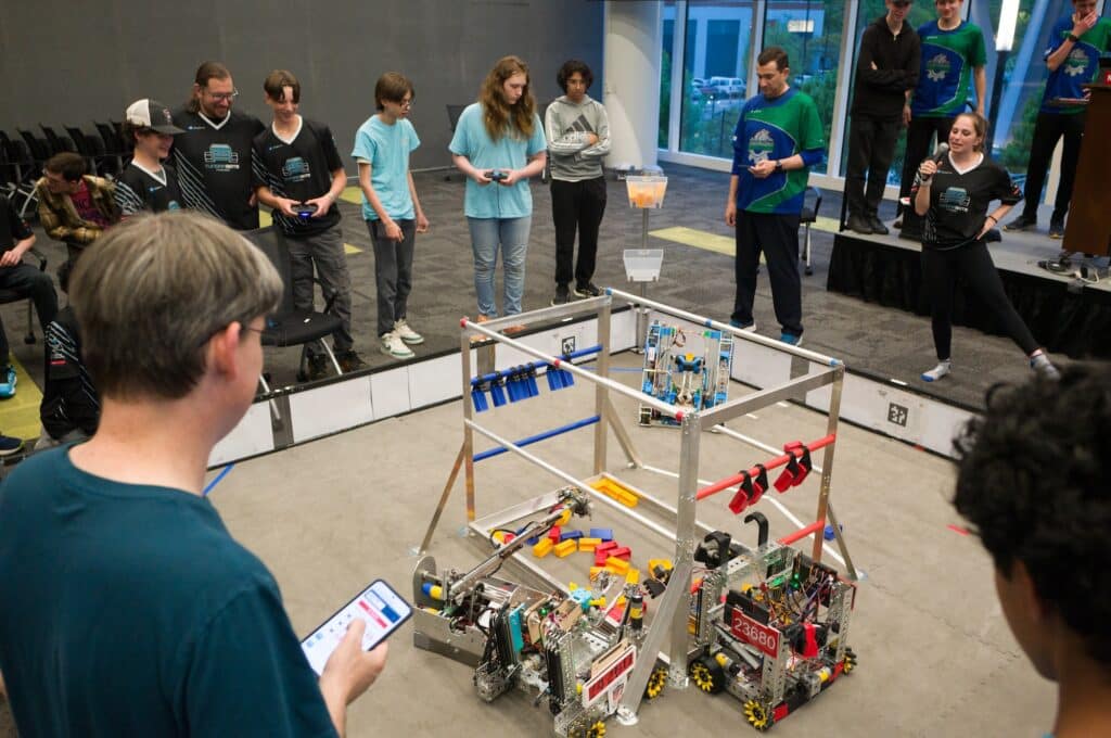 People standing around a group of small, wheeled robots