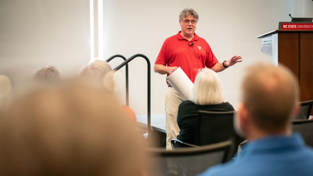 A man in a red shirt speaking near a podium.