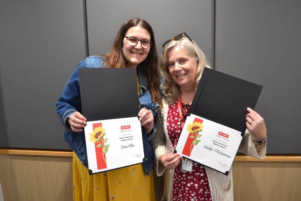 Two people looking at the camera holding their awards