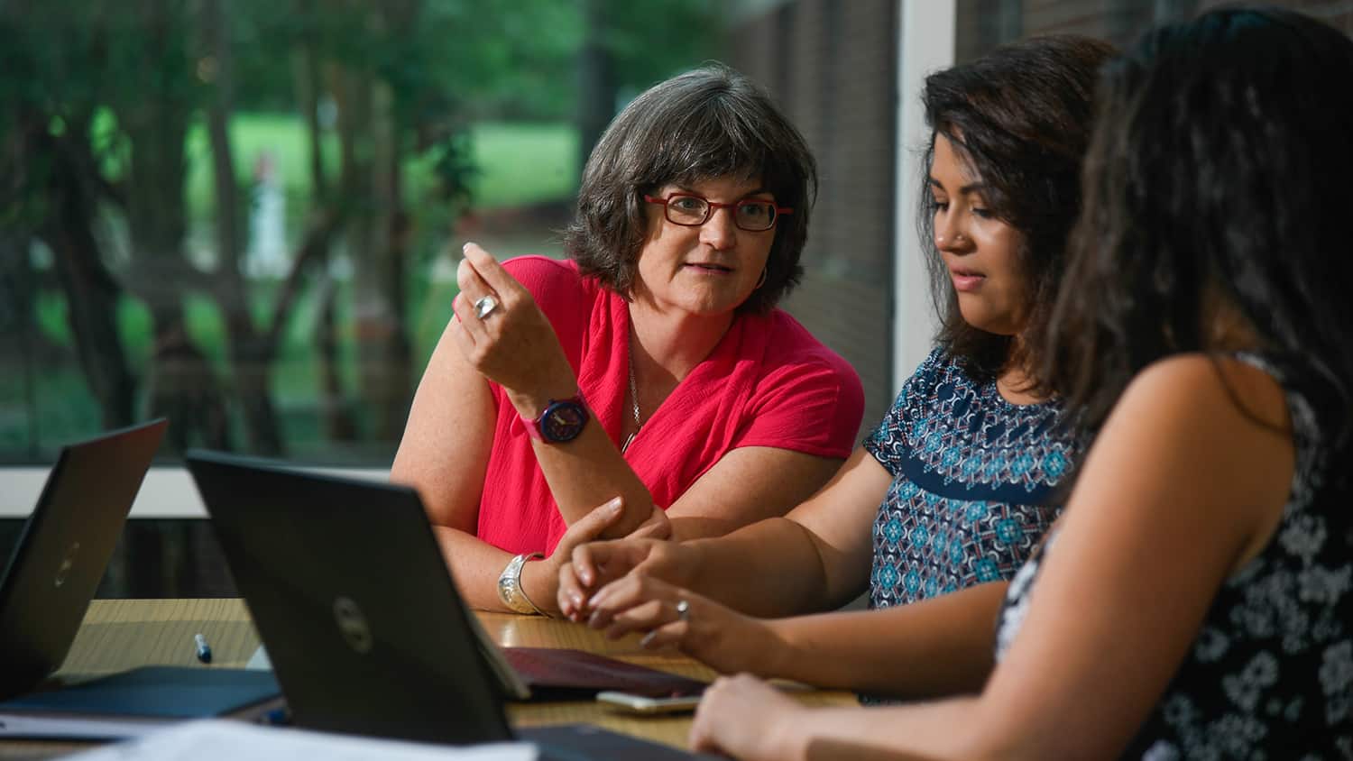 Professor Jane Hoppin speaks with two students sitting at a desk with laptops