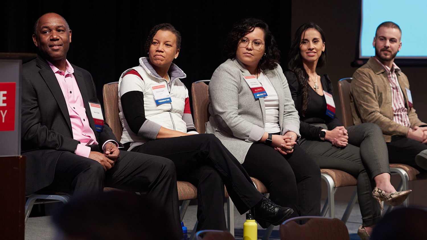 Five panelists at a symposium event sit on stage
