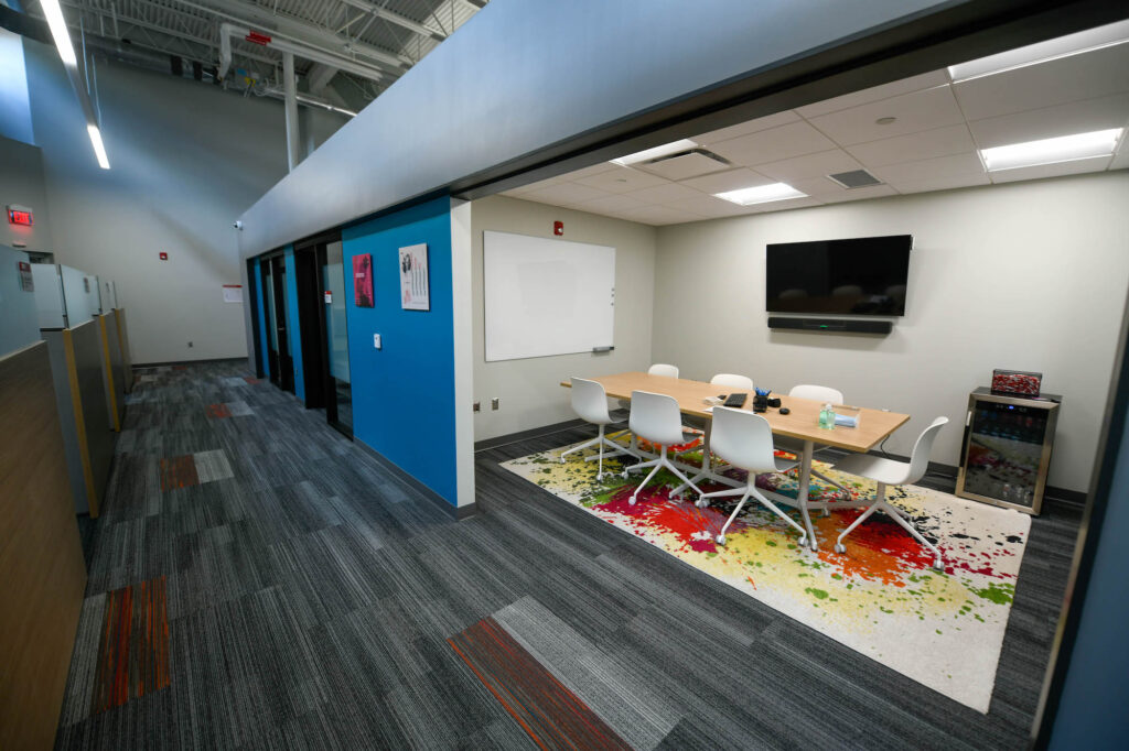 A hallway with cubicles on one side and a conference room and office spaces on the other side. 