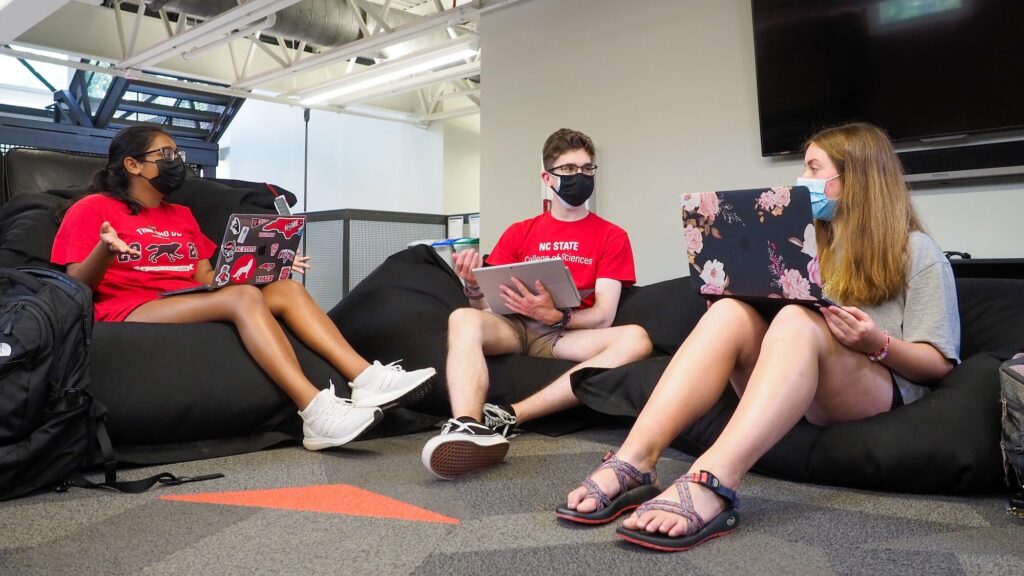 Three students sit on floor pillows in the mezzanine area of the Bureau of Mines building.