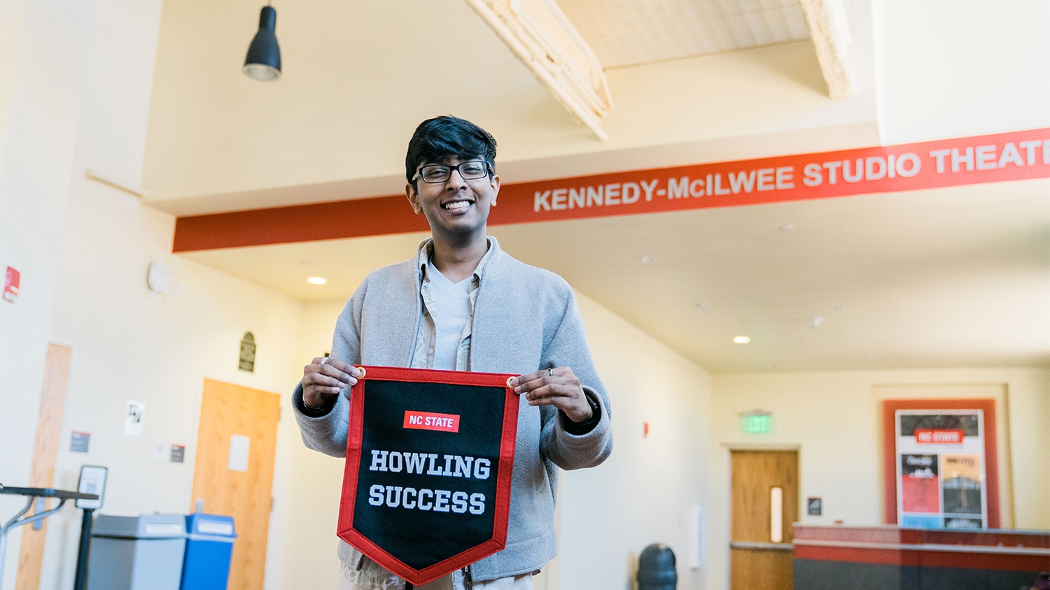Kiran Soma holds a red, white and black banner that reads "Howling Success" in the lobby of Thompson Theatre